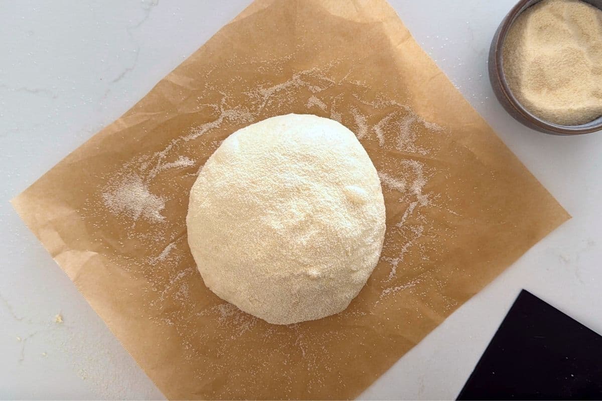 A shaped ball of sourdough discard dough on a square of parchment paper. The dough has been coated in semolina flour to stop it sticking. 