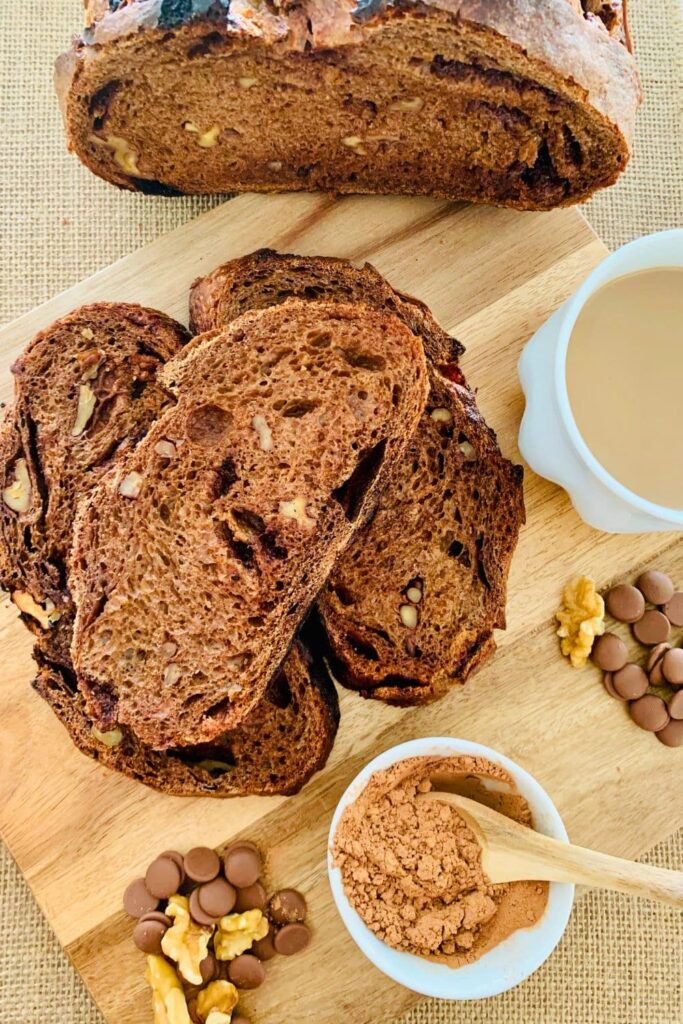 A loaf of chocolate walnut sourdough bread that has been sliced and displayed on a wooden board.