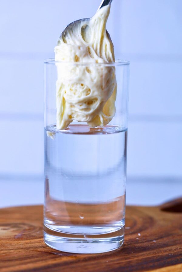 A spoon of bubbly sourdough starter being spooned into a glass of water that is sitting on a wooden board.