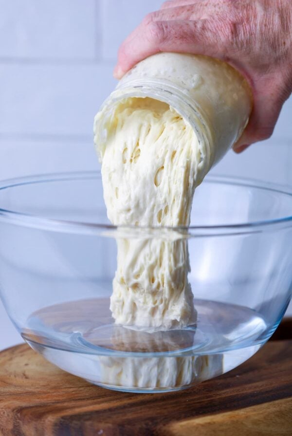 A jar of sourdough starter being poured into a glass bowl of water ready to make sourdough.