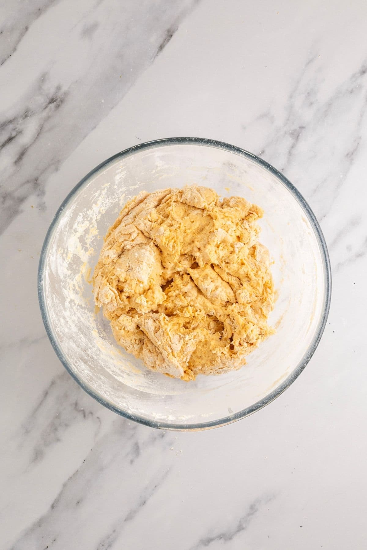 A glass bowl filled with the shaggy dough made by adding the liquid and dry ingredients together.