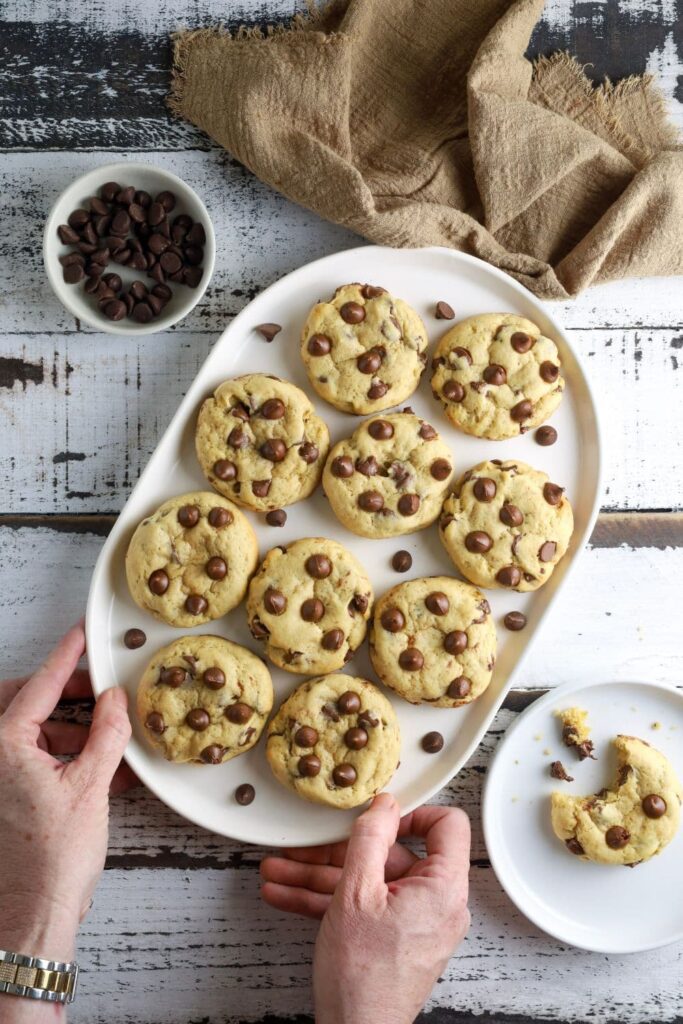 A white oval tray of sourdough chocolate chip cookies overflowing with semi sweet chocolate chips.
