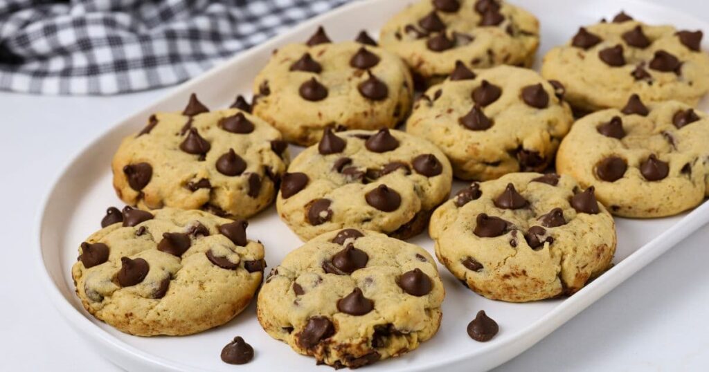 A white oval tray of sourdough chocolate chip cookies overflowing with semi sweet chocolate chips.