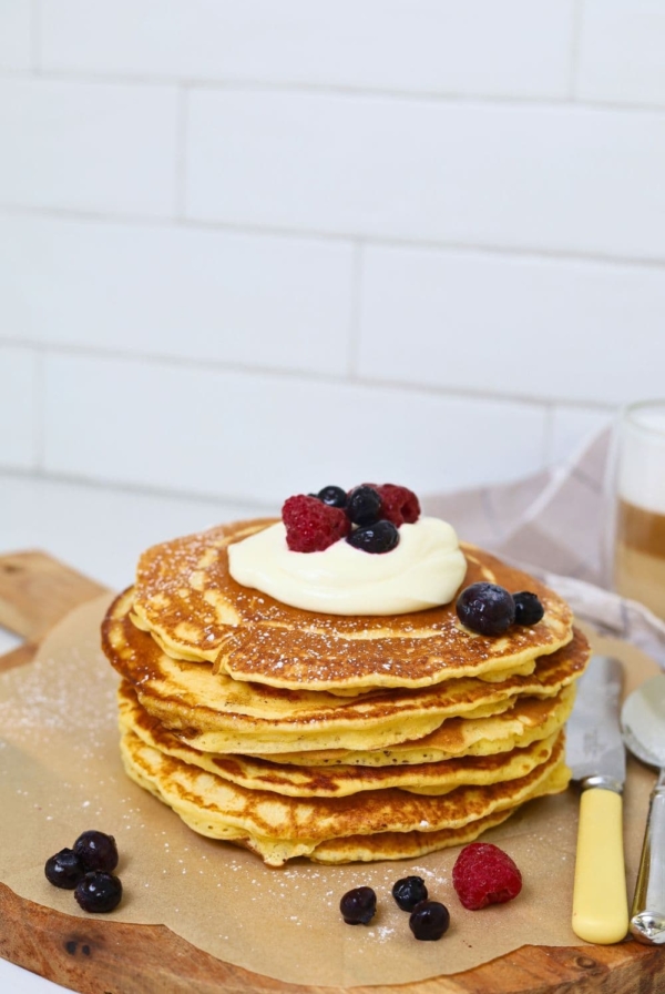 A stack of sourdough discard pancakes topped with whipped cream and berries and drizzled in maple syrup.