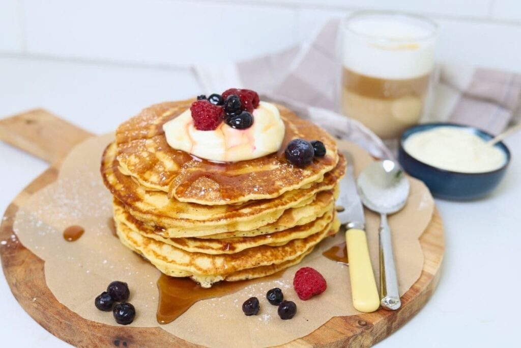A stack of sourdough discard pancakes topped with whipped cream and berries and drizzled in maple syrup.