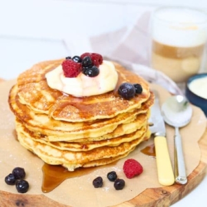 A stack of sourdough discard pancakes topped with whipped cream and berries and drizzled in maple syrup.