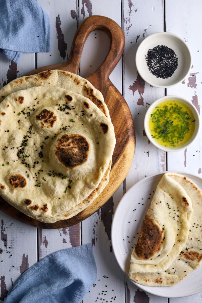 A flatlay photo showing a wooden board holding some sourdough flatbreads. There are some decorative pale blue napkins in the photo.