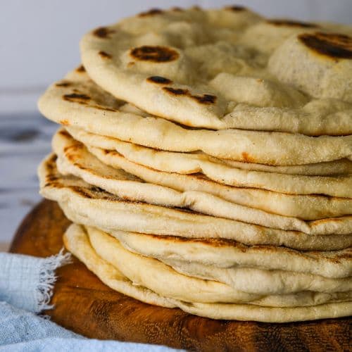 A stack of sourdough flatbreads on a round wooden board.