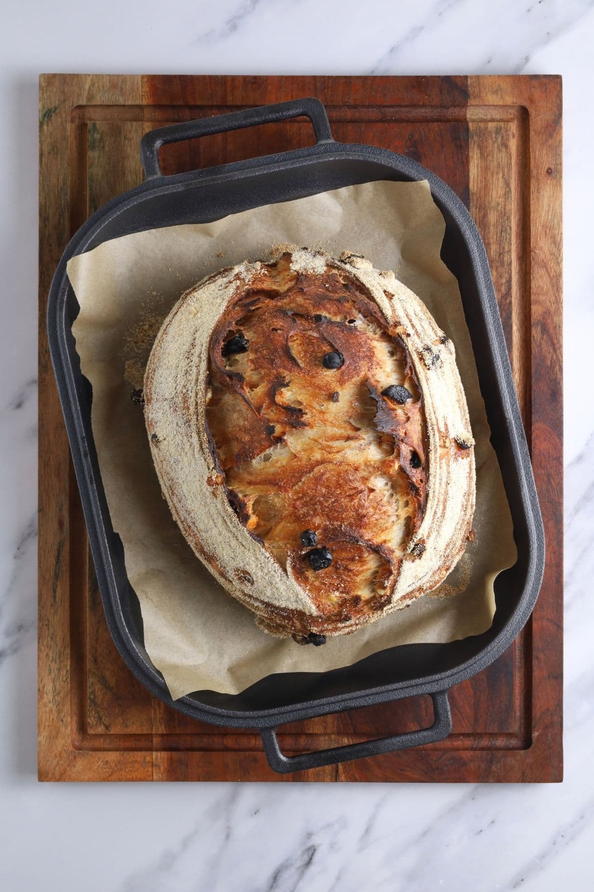 A finished loaf of sourdough fruit bread that has been taken out of the oven and is still sitting in a rectangle cast iron bread pan.