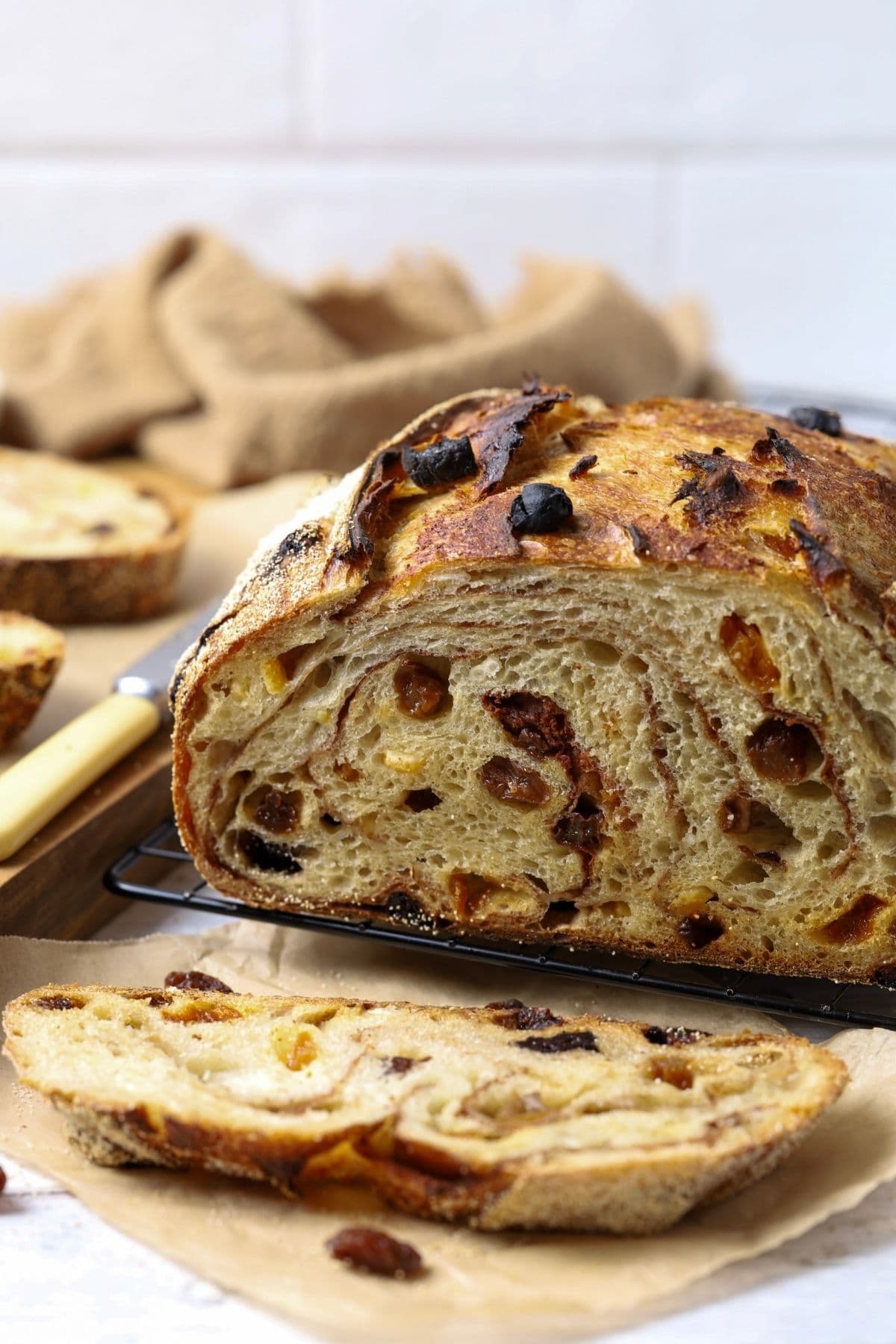A sourdough fruit loaf full of juicy raisins and dried fruit sitting on a counter top with a dish of butter. The loaf has been cut so you can see the cinnamon swirl and raisins inside.
