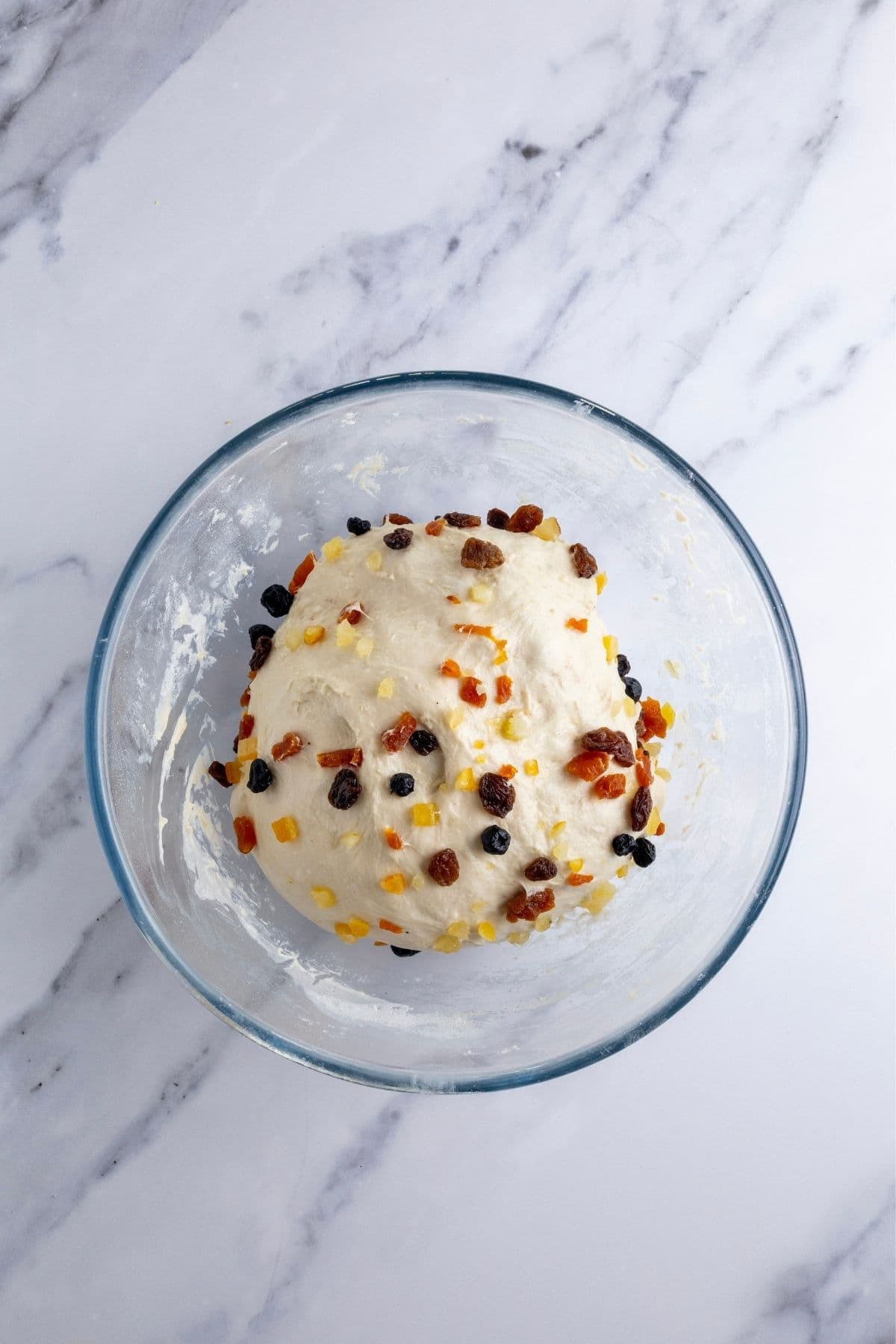 A glass bowl containing sourdough fruit loaf dough. The fruit has been fully incorporated into the dough.