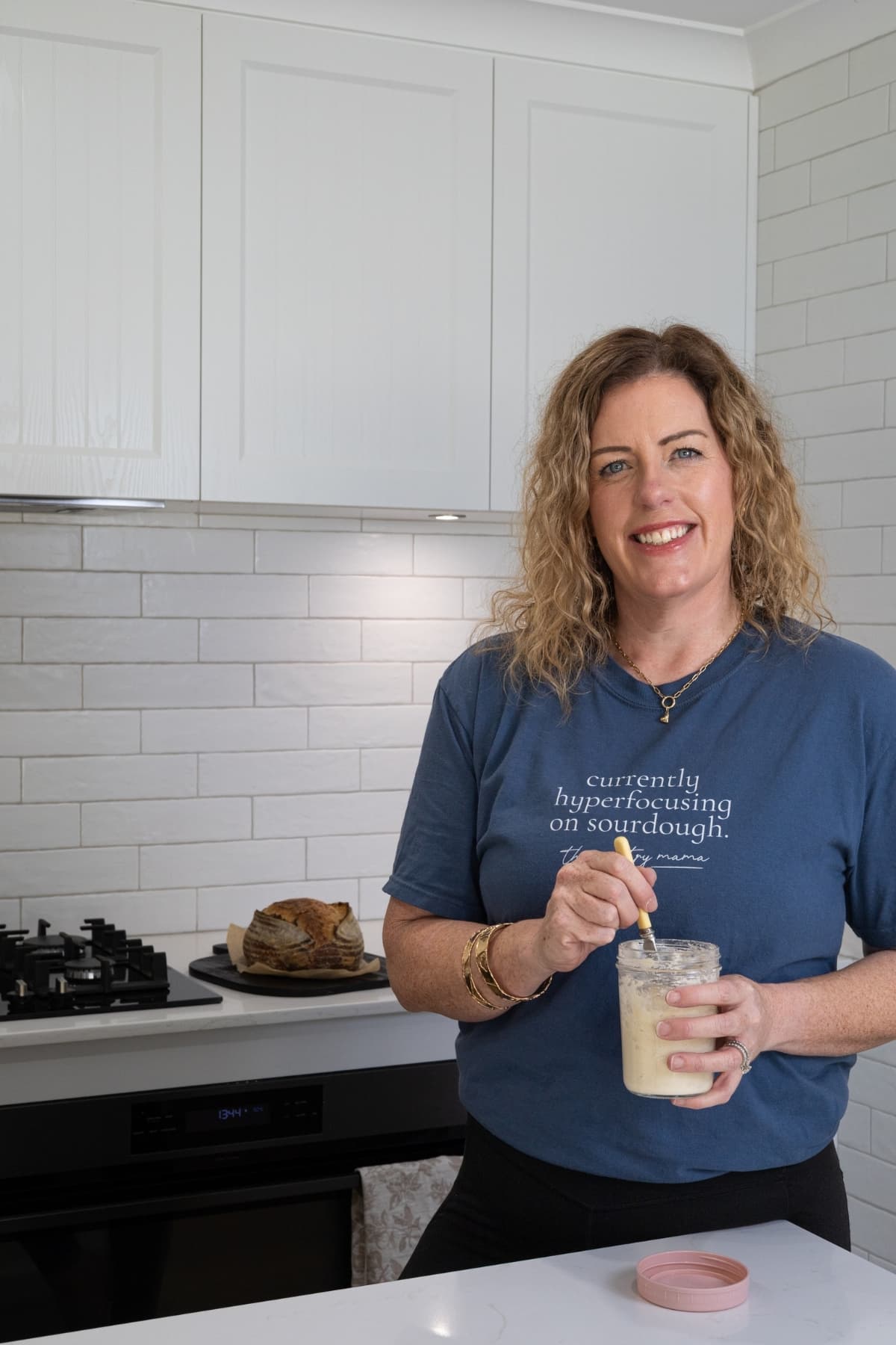 Kate from The Pantry Mama stirring a jar of sourdough starter while wearing a blue t-shirt.