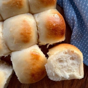 SOURDOUGH DINNER ROLLS ARRANGED WITH A BLUE DISH TOWEL. ONE HAS BEEN TURNED ON ITS SIDE SO YOU CAN SEE THE SOFT CRUMB.