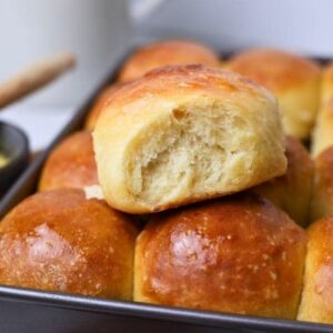 A close up photo of a sourdough Hawaiian roll sitting on top of a tray of more rolls.