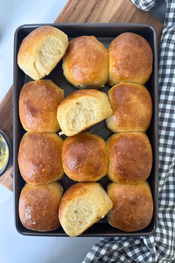 12 sourdough Hawaiian rolls in a metal baking tray. 3 of the rolls have been turned on their sides so you can see the soft crumb inside.