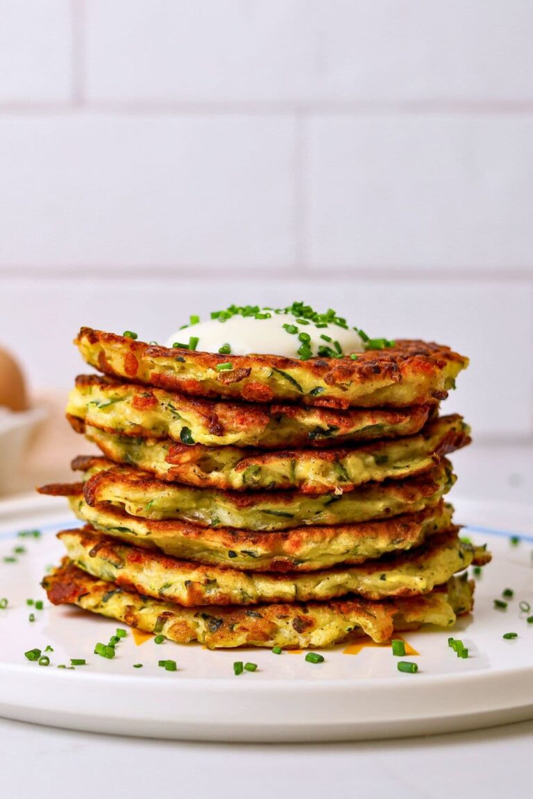 A stack of sourdough zucchini fritters sitting on a plate. There is a carton of eggs in the background of the photo.