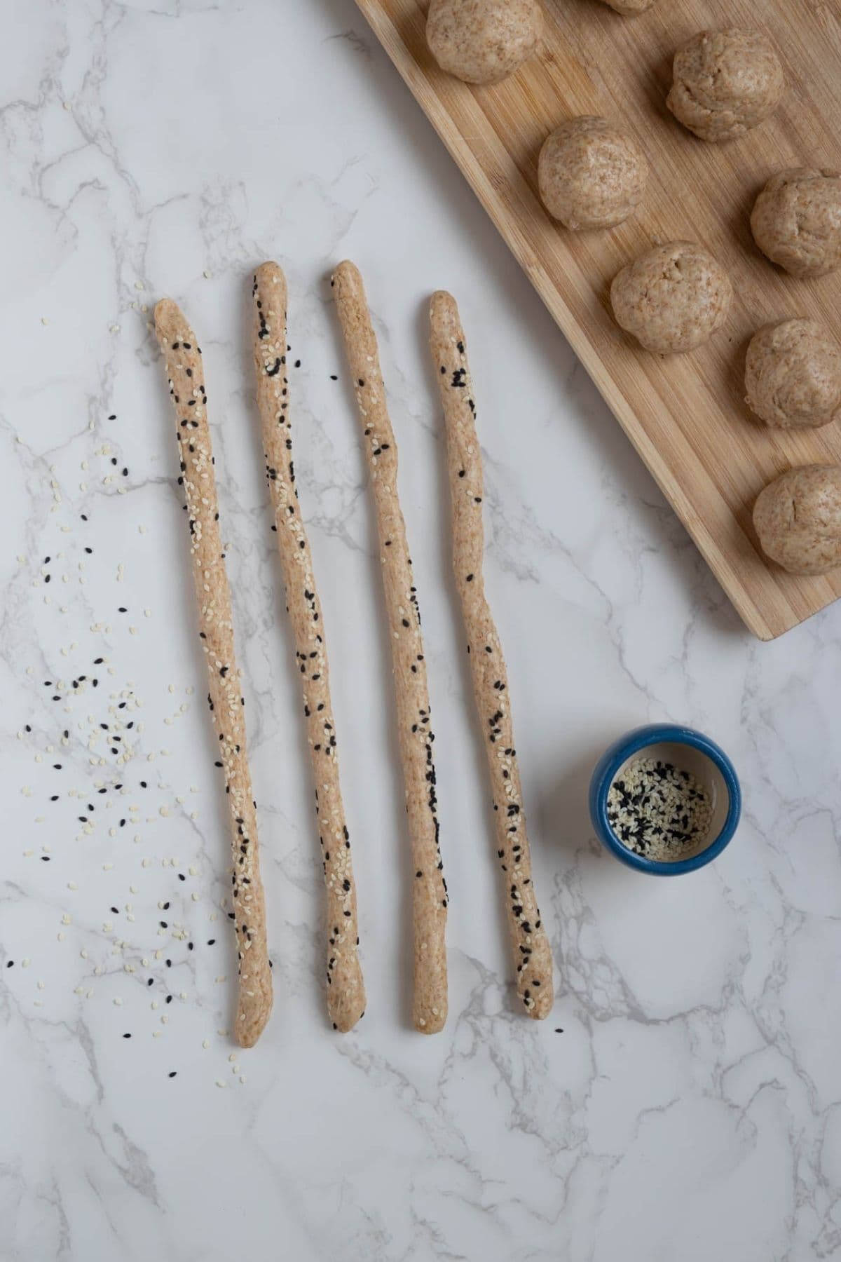 A photo showing how to roll the small bowls of dough into long dough strips, rolled in sesame seeds.