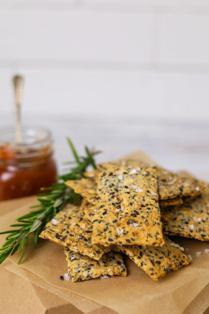 A stack of seeded sourdough crackers displayed on a piece of parchment paper.