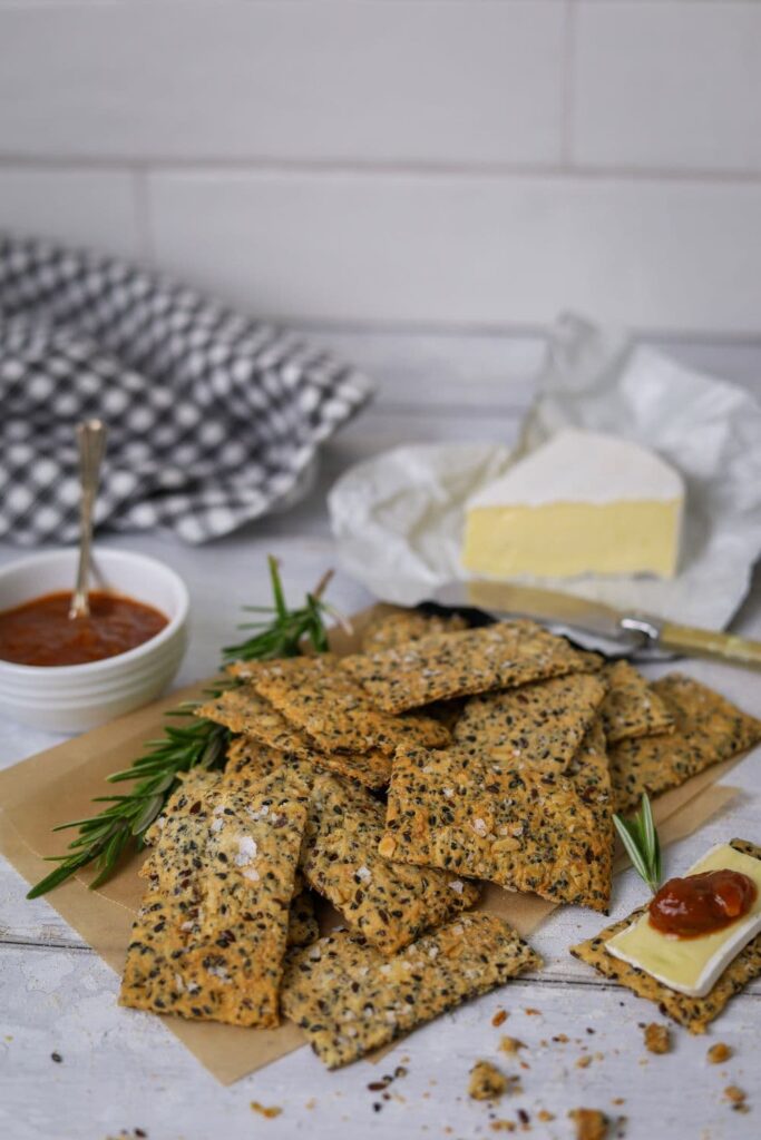 A display of seeded sourdough crackers alongside a small dish of tomato chutney and wedge of Brie.