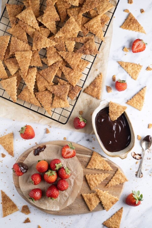 A flat lay image of a batch of sweet cinnamon sourdough crackers cooling on a wire rack. There are bright red strawberries and a bowl of chocolate ganache to accompany the crackers.