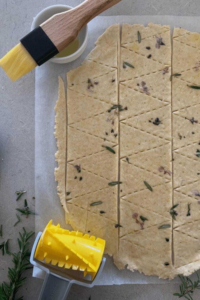 Sourdough cracker recipe dough rolled out thin and sprinkled with rosemary and salt. It has been cut with a cracker roller which is also shown in the photo.