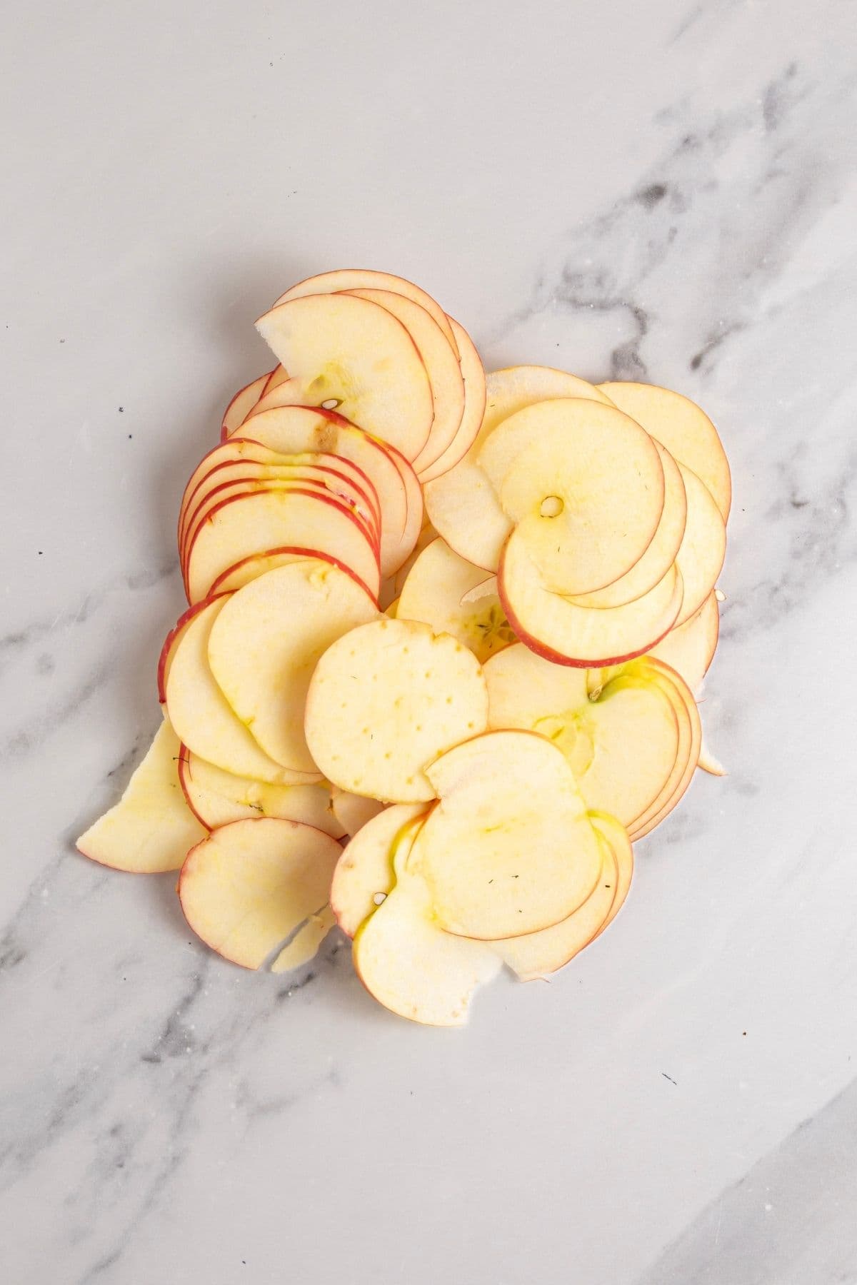 A pile of apples that have been finely sliced using a mandoline. They still have the peel on the outside.