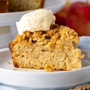 A single slice of sourdough apple cake placed on a white plate and topped with a dollop of whipped cream.