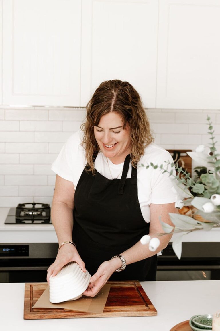 Kate from the Pantry Mama taking dough out of a banneton basket onto a sheet of parchment paper. This is the feature image for the blog banneton sizing guide.