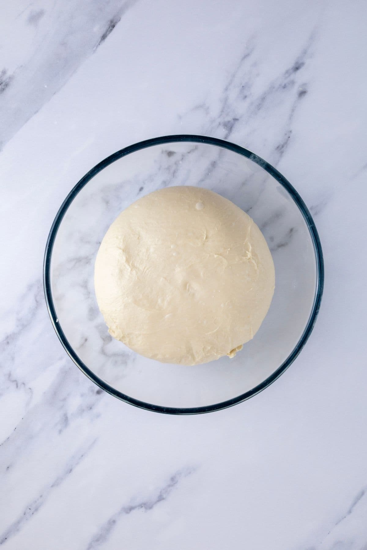 A bowl of sourdough hot dog bun dough that has risen around 50% during bulk fermentation.