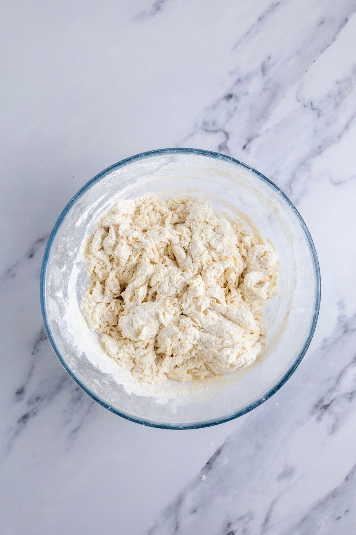 A glass bowl containing shaggy dough to make sourdough hot dog buns.