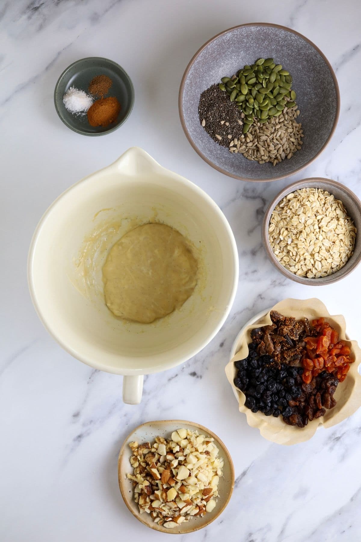 Wet ingredients for the granola blended together in a batter jug. The dry ingredients are laid out on the counter top surrounding the jug of wet ingredients.
