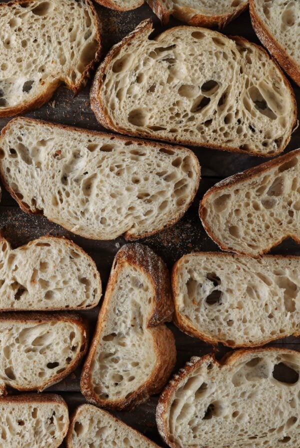 Lots of slices of sourdough bread laid out on a wooden board so you can see the open crumb inside.