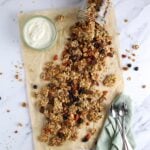 A flat lay image of homemade sourdough granola spilling out of a jar onto a piece of parchment paper.