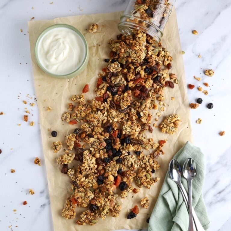 A flat lay image of homemade sourdough granola spilling out of a jar onto a piece of parchment paper.