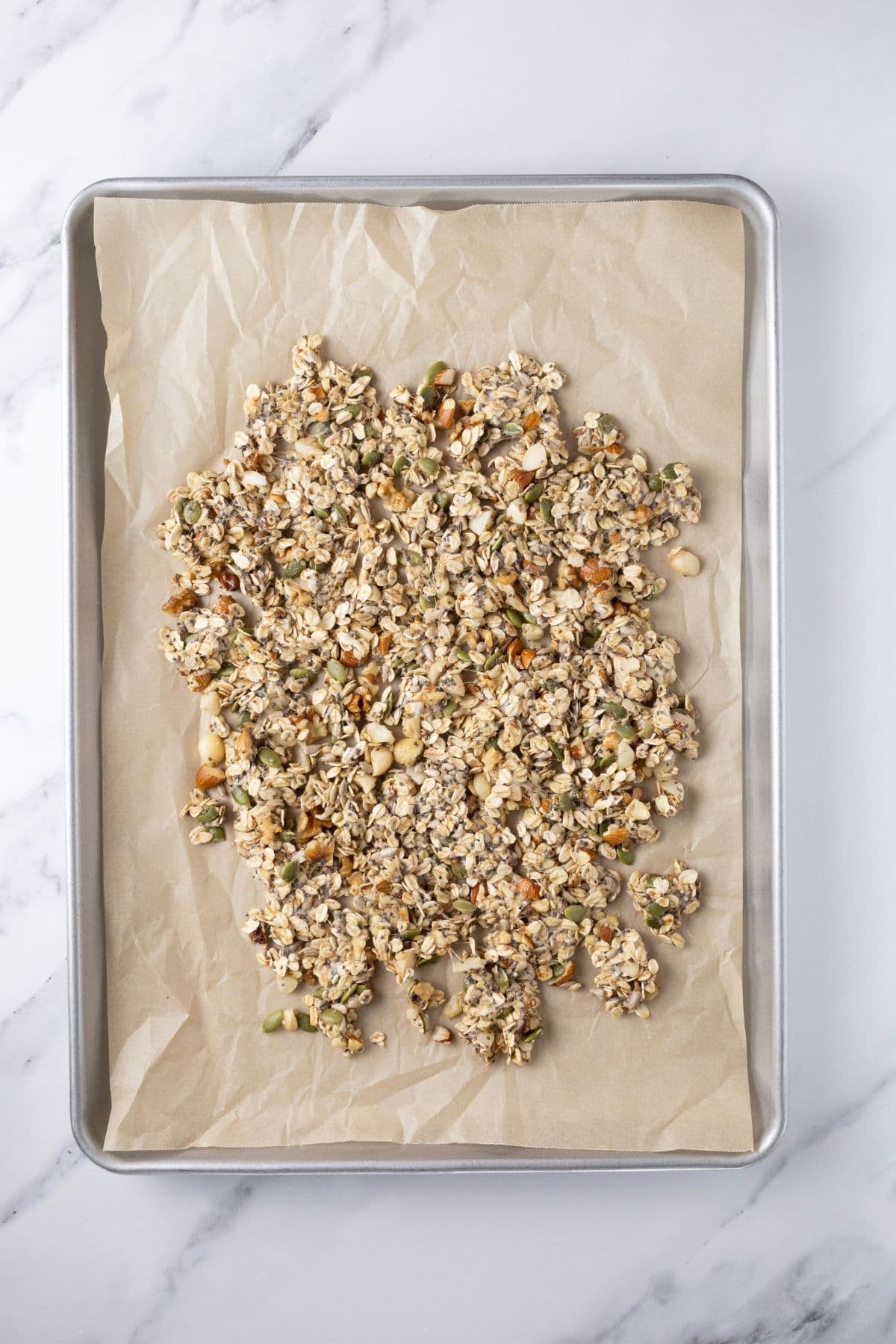 Sourdough granola spread out tightly onto a parchment lined baking sheet ready to go into the oven to bake. There is no dried fruit in the sourdough granola as this is added later.