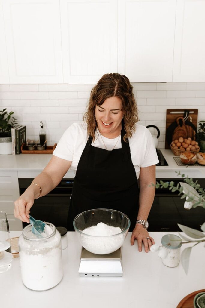 Kate from The Pantry Mama scooping bread flour from a glass jar into a glass bowl.