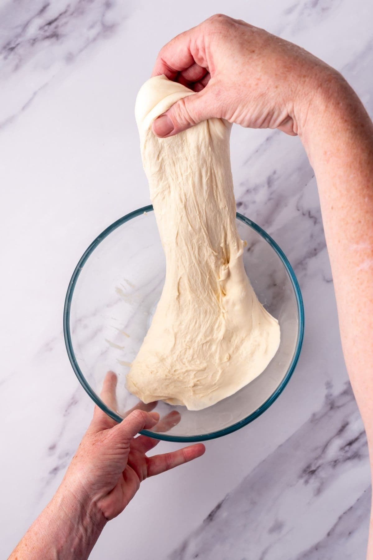 A photo showing sourdough dough being stretched in a glass bowl.