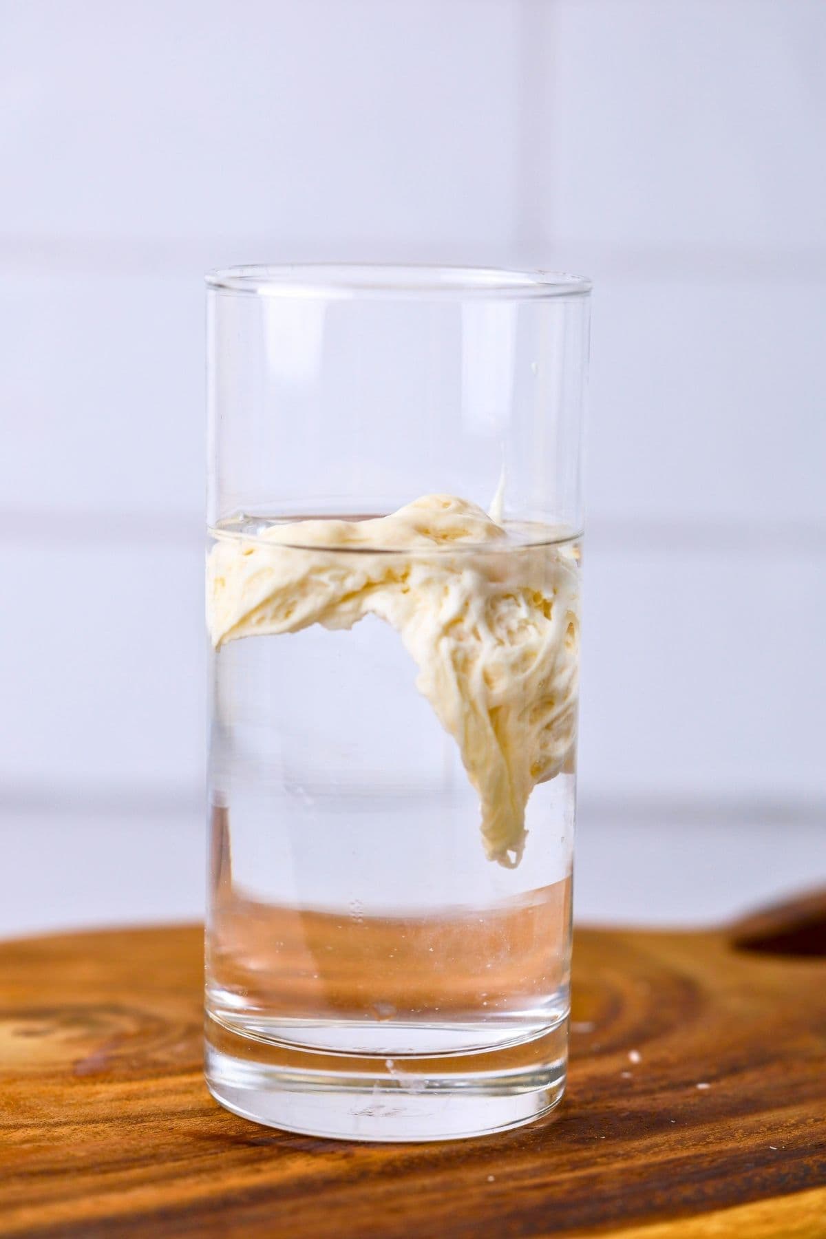 A scoop of sourdough starter floating in a glass of water to demonstrate the sourdough float test.