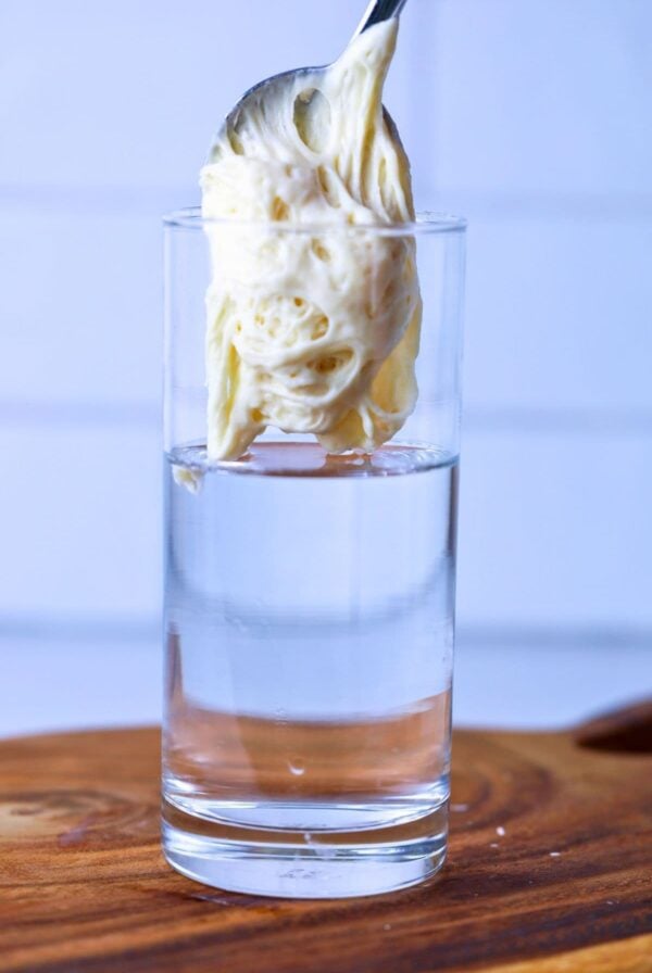 A scoop of sourdough starter on a spoon being dropped into a tall glass of water.