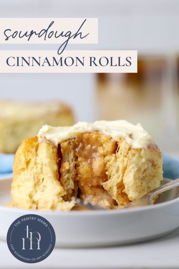 Sourdough Cinnamon Rolls Pinterest Image - A sourdough cinnamon roll sitting on a white plate. The cinnamon roll is filled with gooey cinnamon brown sugar filling and topped with vanilla cream cheese filling. You can see a cup of coffee in the background, as well as a light blue napkin.