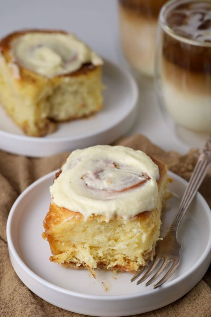 A close up photo of two sourdough cinnamon rolls sitting on a latte colored linen napkin with two glass cups of coffee.