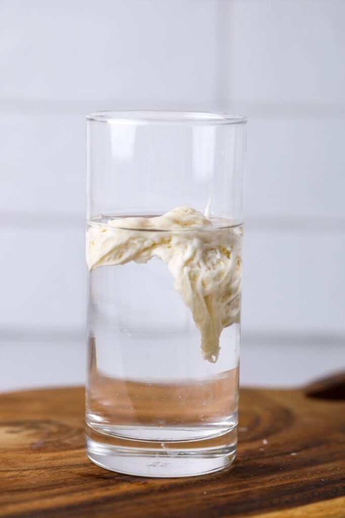 A scoop of sourdough starter floating in a glass of water to demonstrate the sourdough float test.
