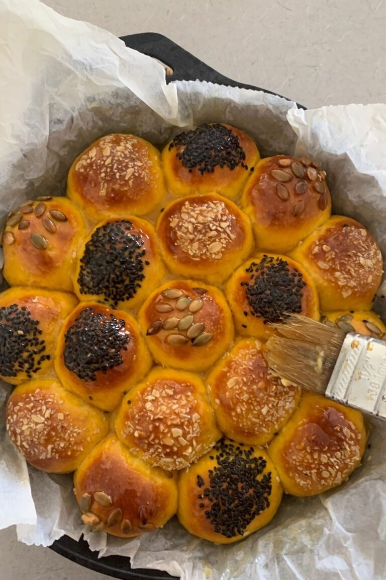 Sourdough pumpkin dinner rolls fresh out of the oven and being brushed with honey butter using a pastry brush