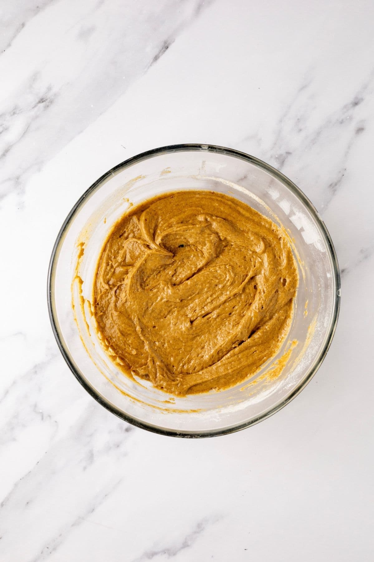 A glass bowl filled with sourdough gingerbread muffin batter that has been stirred together.