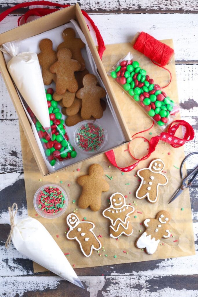An image of a box filled with a piping bag of royal icing, Christmas M&Ms, Christmas sprinkles and sourdough gingerbread men. There are some gingerbread cookies decorated with royal icing next to the box.