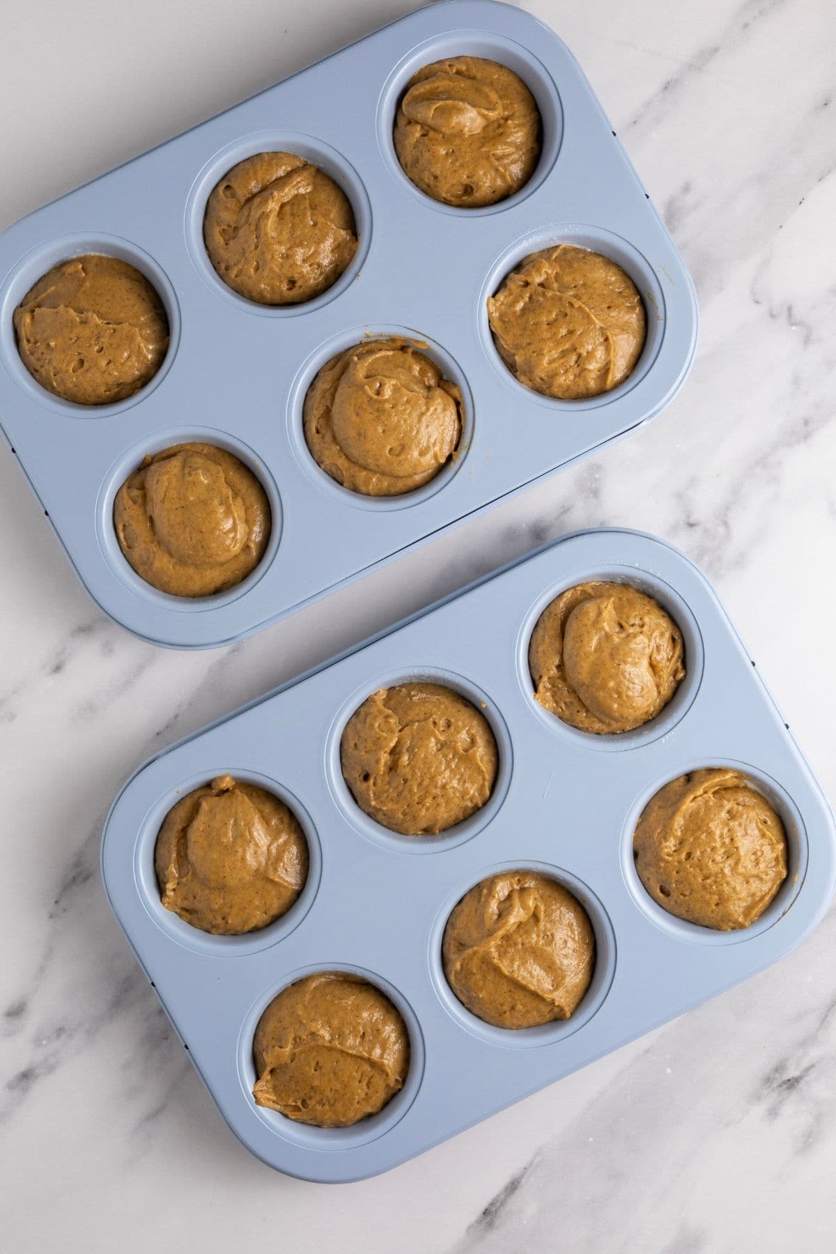Two pale blue 6 hole muffin pans filled with sourdough gingerbread muffin batter.
