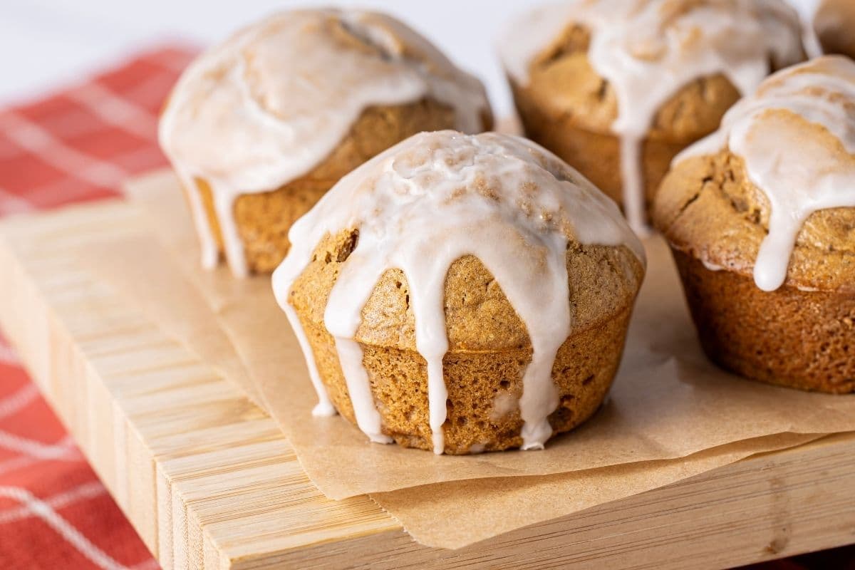 4 sourdough gingerbread muffins drizzled in a white sugar glaze. The muffins are sitting on a wooden board that is on top of a red checkered dish towel.