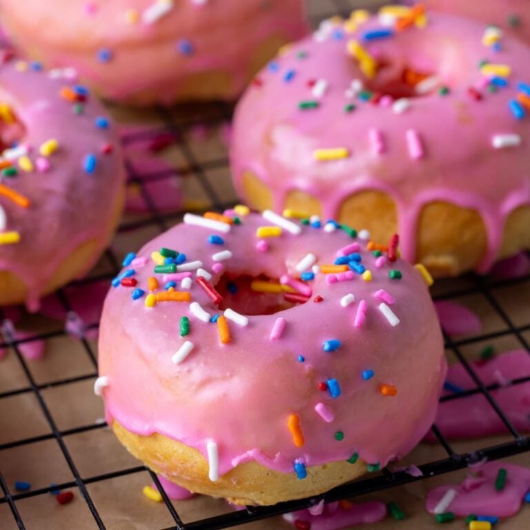 A close up photo of baked sourdough donuts drizzled in pink glaze and sprinkles.