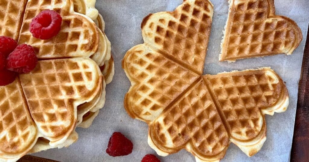 Sourdough discard waffles cooked in a round waffle maker topped with maple syrup and raspberries.