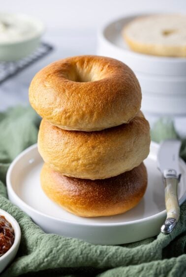 A stack of 3 golden brown sourdough bagels sitting on a white plate.